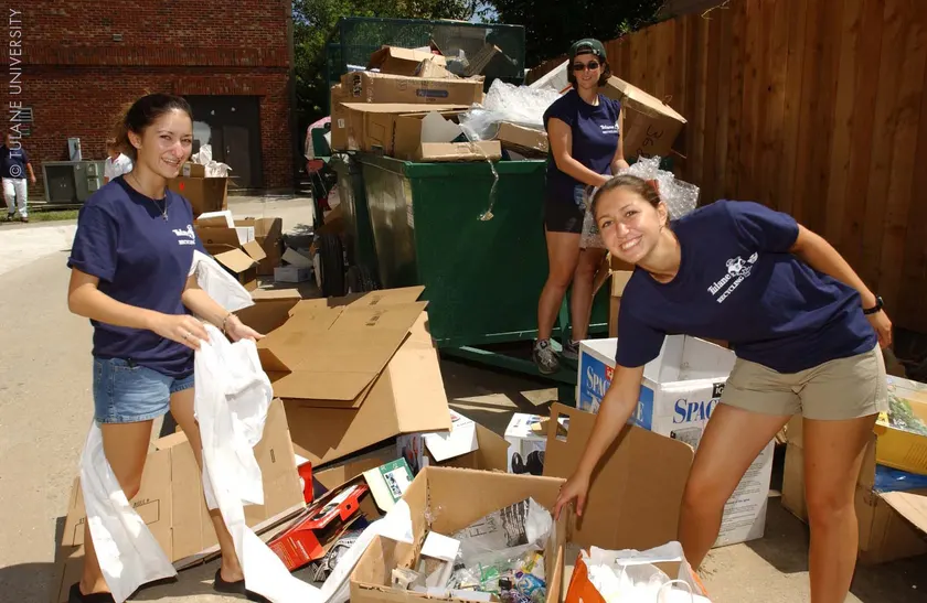 Three college-age volunteers sorting boxes of recyclables beside a loaded dumpster