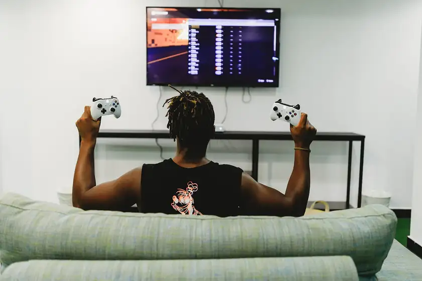 A person seen from behind holding two game controllers toward a television