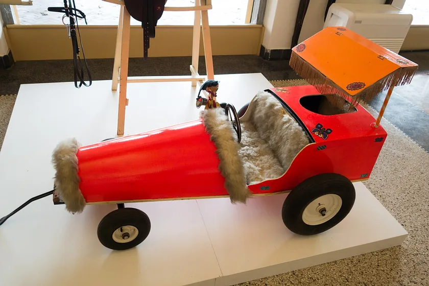 A vintage red pedal car with whitewall tires on display indoors
