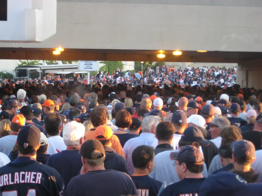 A dense crowd of football fans in a stadium, many in blue and orange, with arms raised