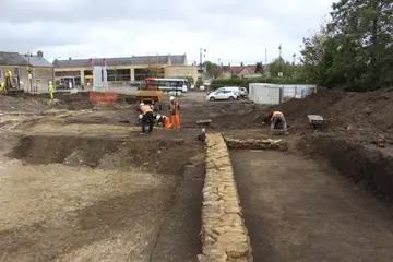 Archaeologists in high-visibility clothing excavating a stone wall