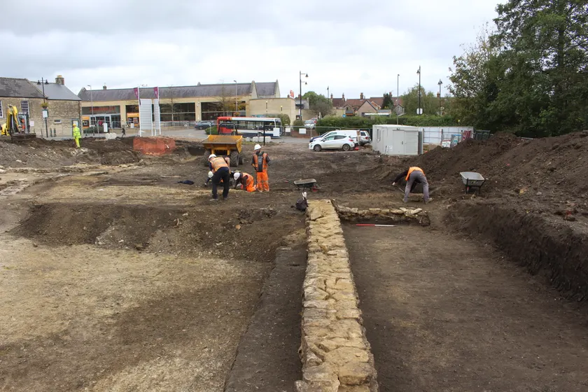 Archaeologists in high-visibility clothing excavating a stone wall