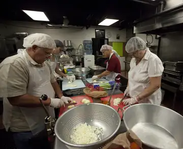 People in a kitchen preparing pans of food to share
