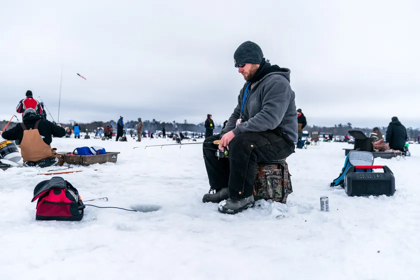 A crowd of people ice fishing on a frozen lake, with huts and lines set over the ice