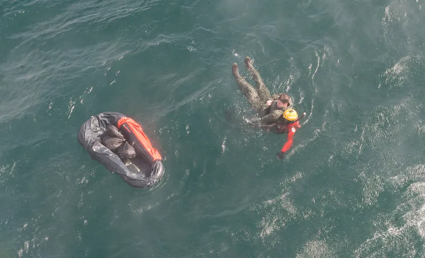 A rescue swimmer in a red suit moves through open water beside a small raft