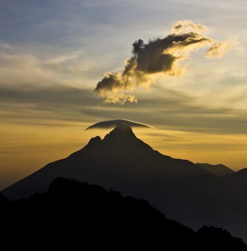 A forested volcanic peak rising above a green valley