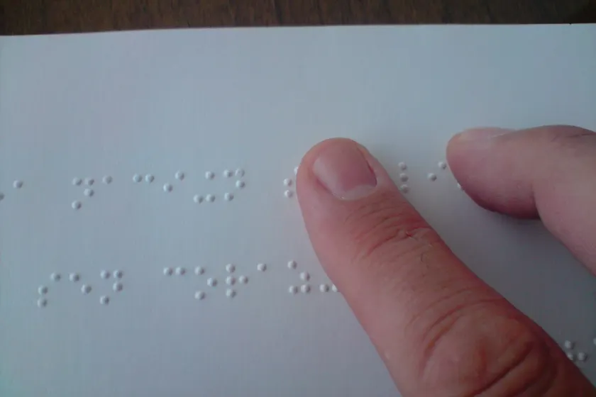 An adult's hands reading a page of braille, with raised dots under the fingertips