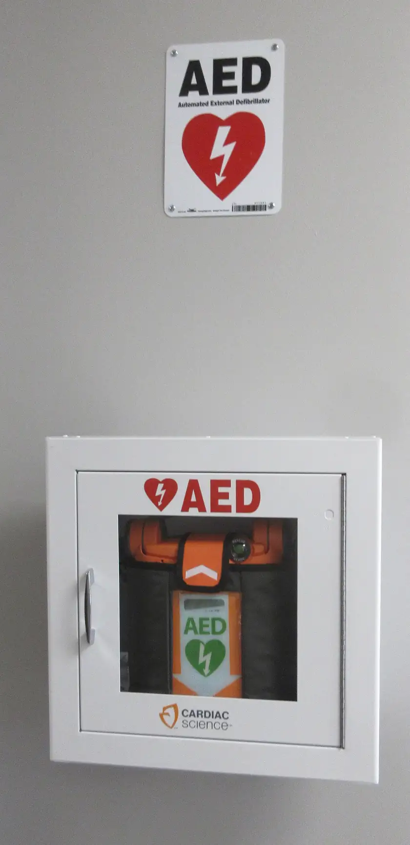 An automated external defibrillator inside a wall cabinet under a sign