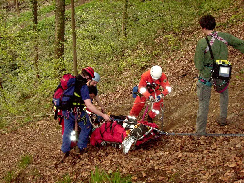 Rescuers carrying a person on a mountain stretcher along a rocky slope