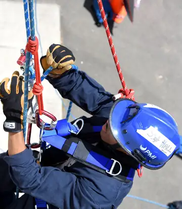 Firefighters in helmets rappelling down a training wall on ropes