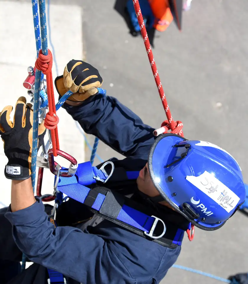 Firefighters in helmets rappelling down a training wall on ropes