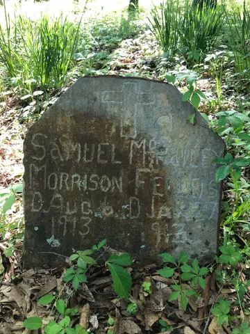 Weathered headstones and an American flag in a grassy historic cemetery