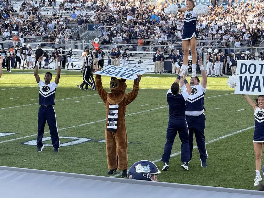 Cheerleaders and a mascot leading a crowd at a packed college football stadium