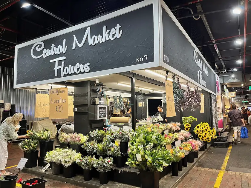 Adults arranging buckets of cut flowers at an indoor market stall