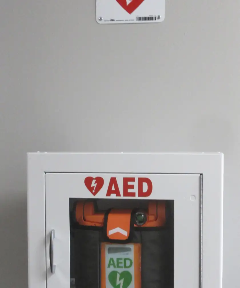 An automated external defibrillator inside a yellow wall cabinet