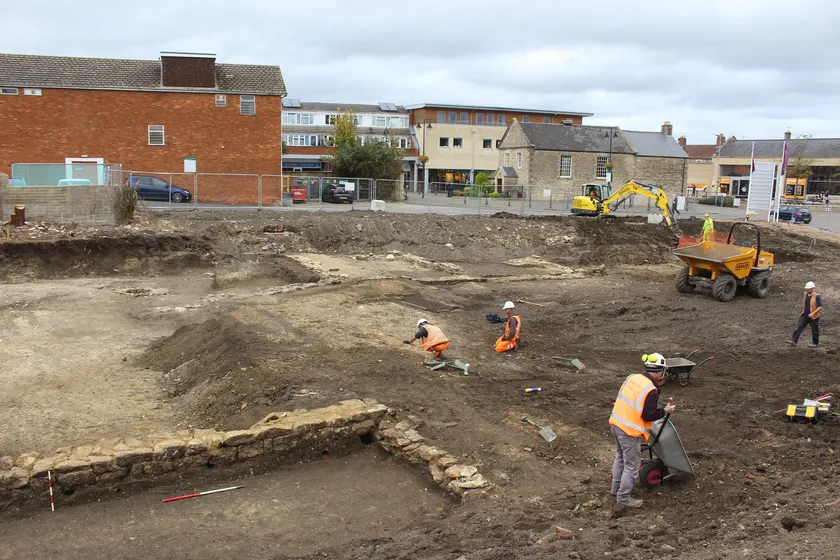 Archaeologists in high-visibility clothing working in an open excavation with stone walls exposed