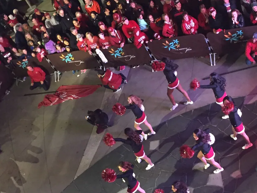 Students in red and white cheering at a pep rally, seen mostly from behind