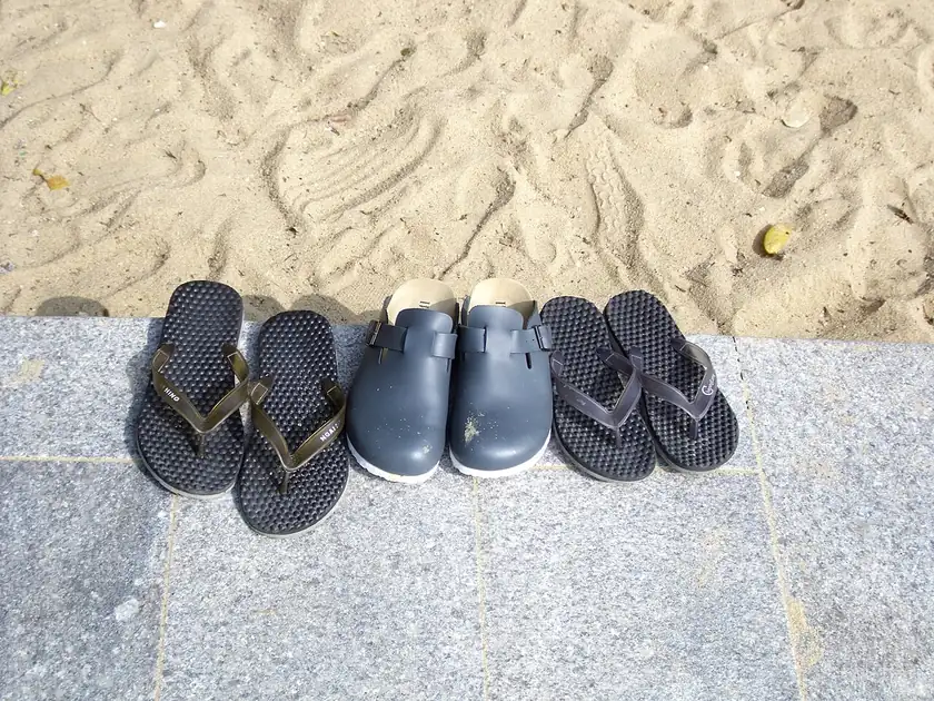 Black flip-flops and a pair of leather sandals on sand