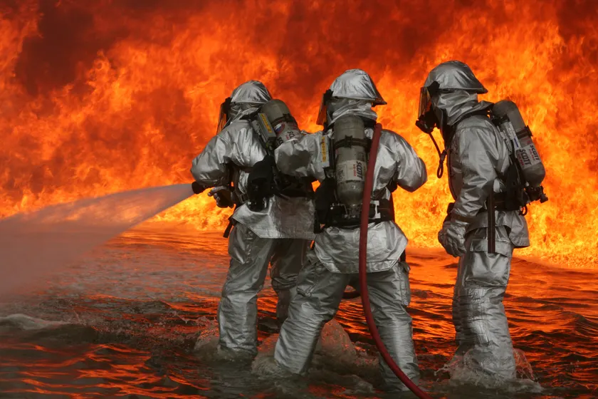 Firefighters in protective gear spraying a hose at flames