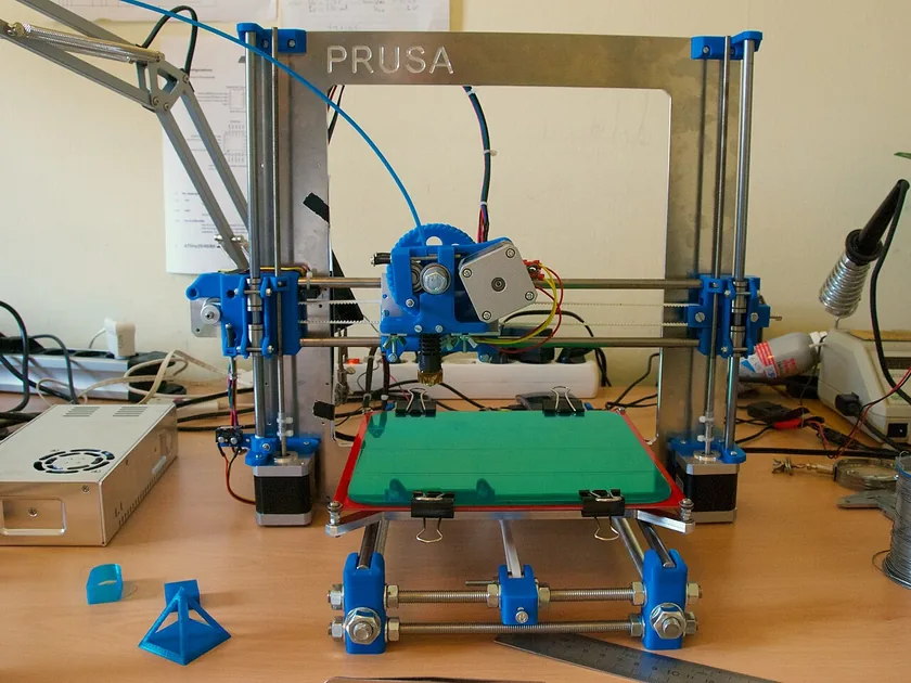 A white Prusa i3 3D printer with a spool of filament on a desk