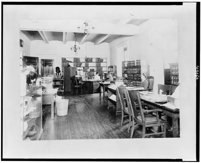 People working at desks in a reading room lined with books