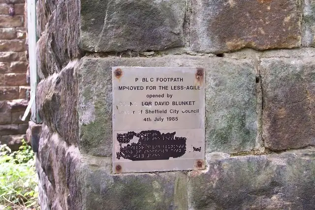 A wooden trail sign that includes a braille panel, with no people