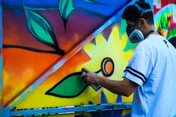 An artist in a mask spray-painting a colorful flower mural