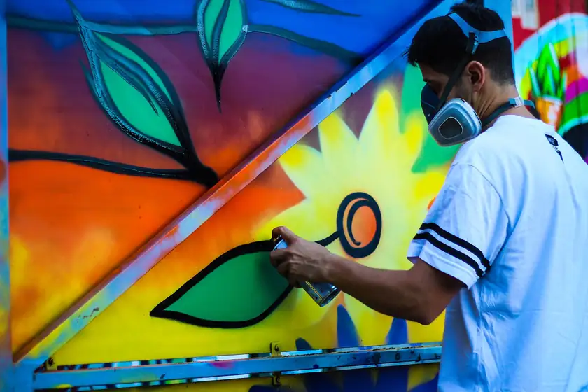 An artist in a mask spray-painting a colorful flower mural