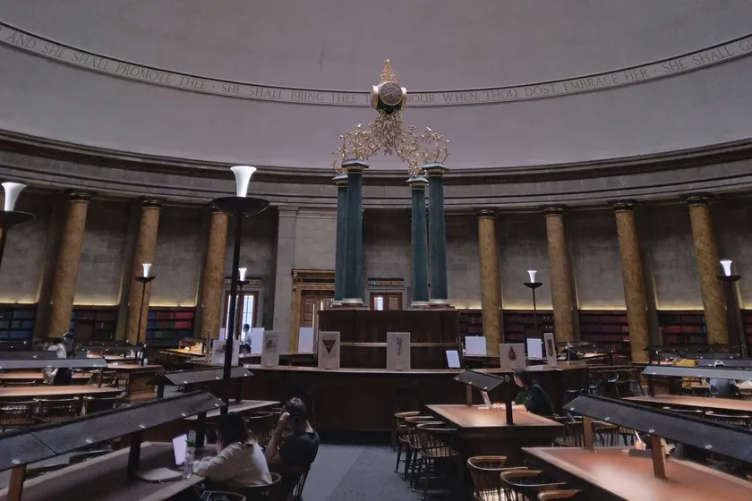 Adults studying at long wooden tables in a grand library reading room