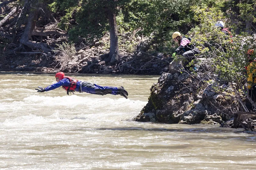 Rescue trainees in helmets and life jackets paddling a blue raft through whitewater