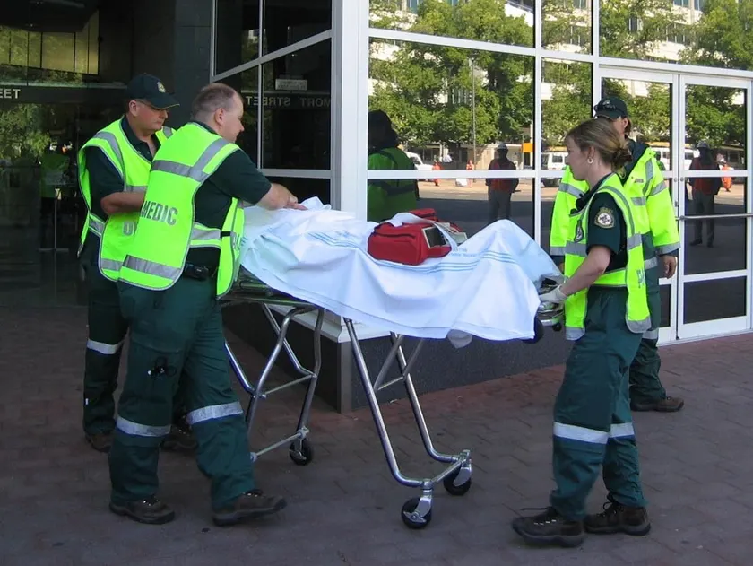 Two paramedics in yellow uniforms wheeling a patient on a stretcher