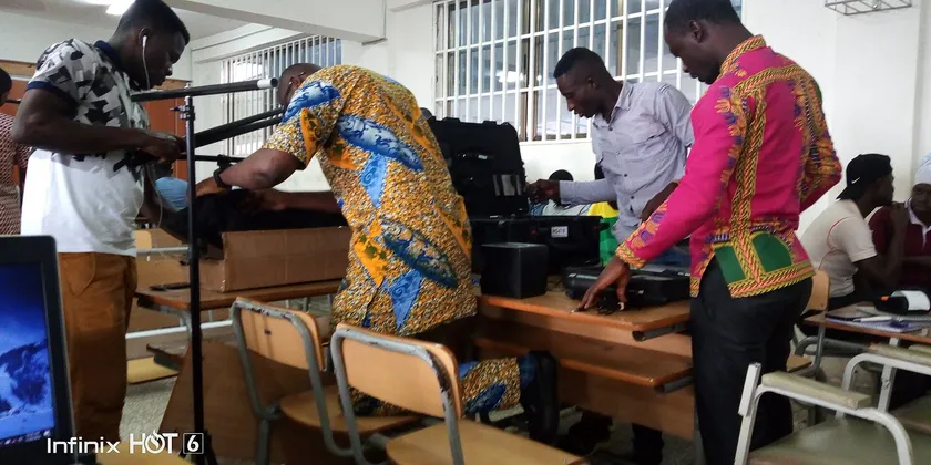 University students seated in rows in a lecture hall, some raising their hands