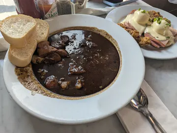 A restaurant plate with eggs, potatoes, fruit, and toast on a wooden table