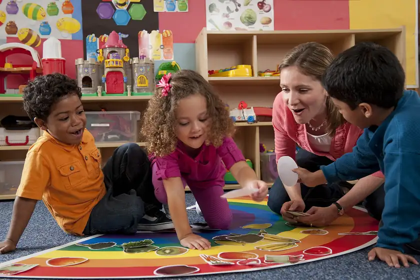 A teacher with young children seated on the floor of a classroom, faces turned away