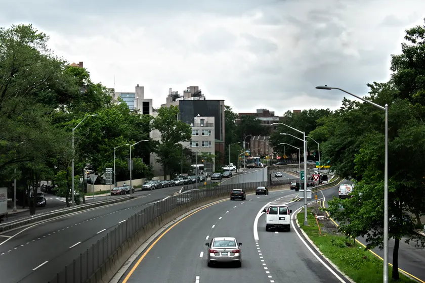 The Henry Hudson Parkway in daylight, curving beside trees and apartment buildings