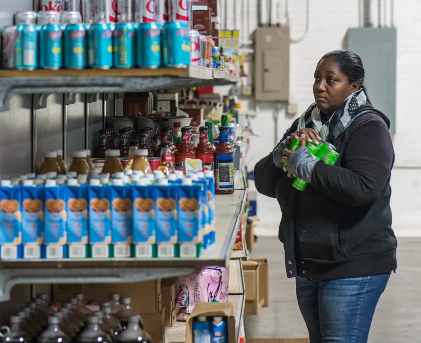 Two women in a food-bank warehouse packing canned goods into cardboard boxes