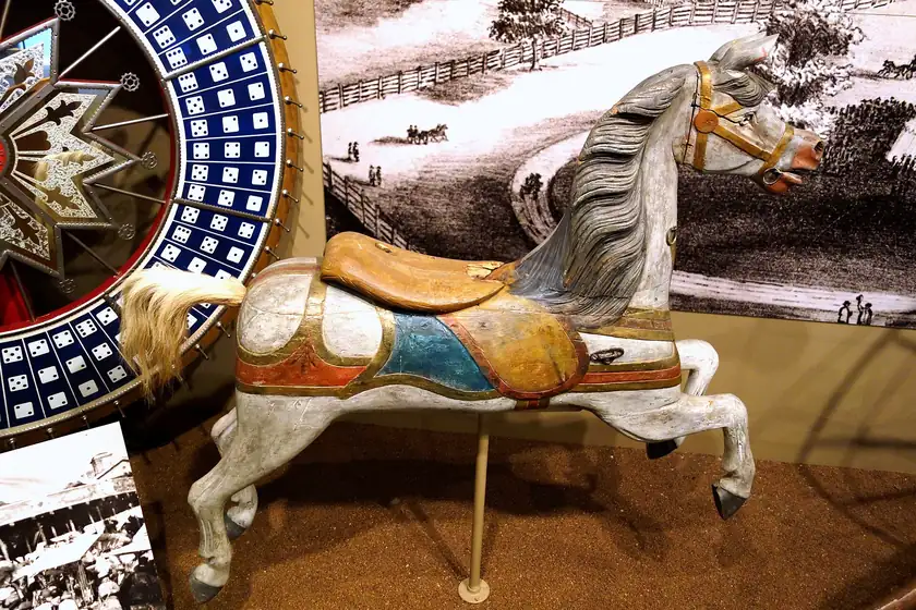 A carved wooden carousel horse with a red saddle, displayed indoors