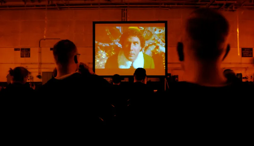 People seated in a dark room watching a movie on a large screen