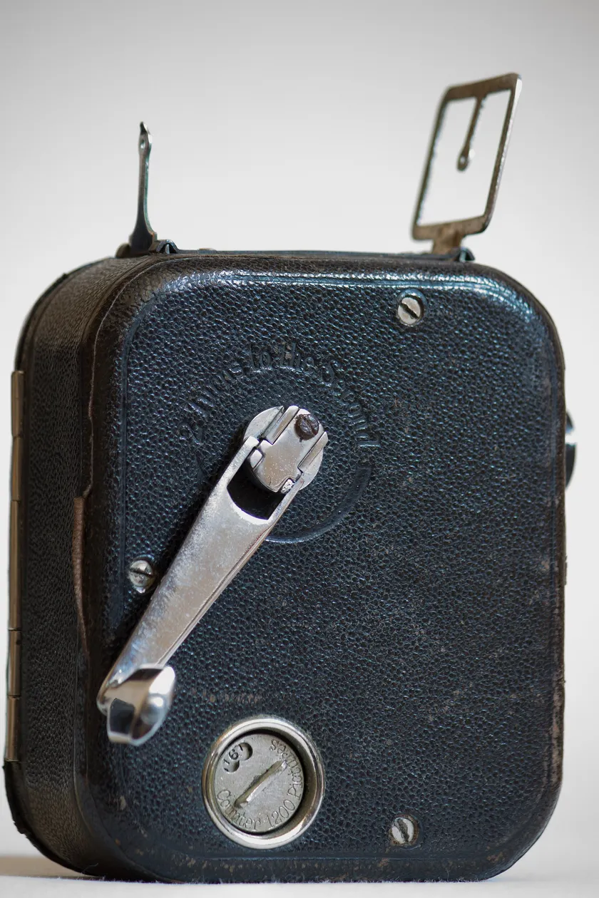 A small vintage hand-crank movie camera standing on a white surface