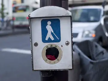 A person seen from behind using a white cane to cross a city street