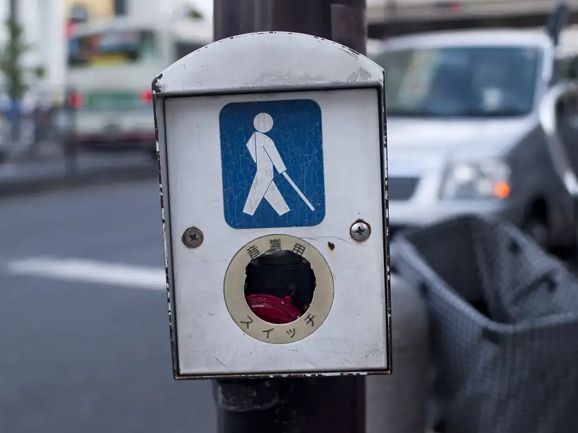 A person seen from behind using a white cane to cross a city street