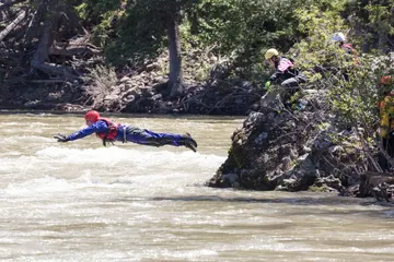 Two rescuers in helmets and dry suits paddling a yellow raft through whitewater