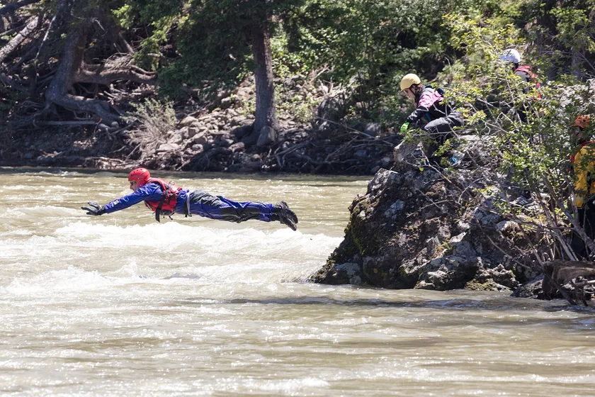 Two rescuers in helmets and dry suits paddling a yellow raft through whitewater