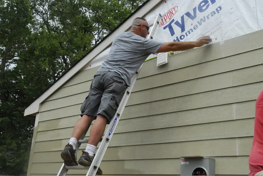 A man on a ladder installing siding on the side of a house