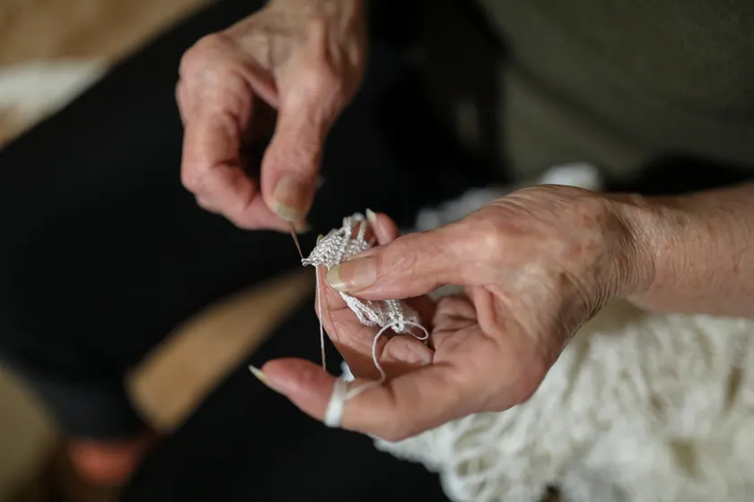 An older person's hands crocheting white lace