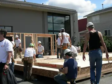 Volunteers in red shirts building a wooden frame at an outdoor fair