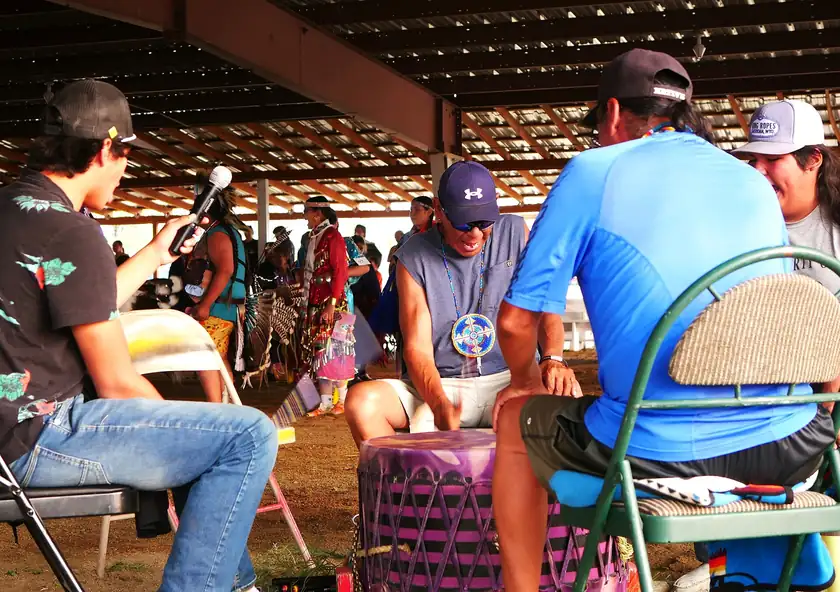 People seated around a large drum outdoors, with faces not clearly shown