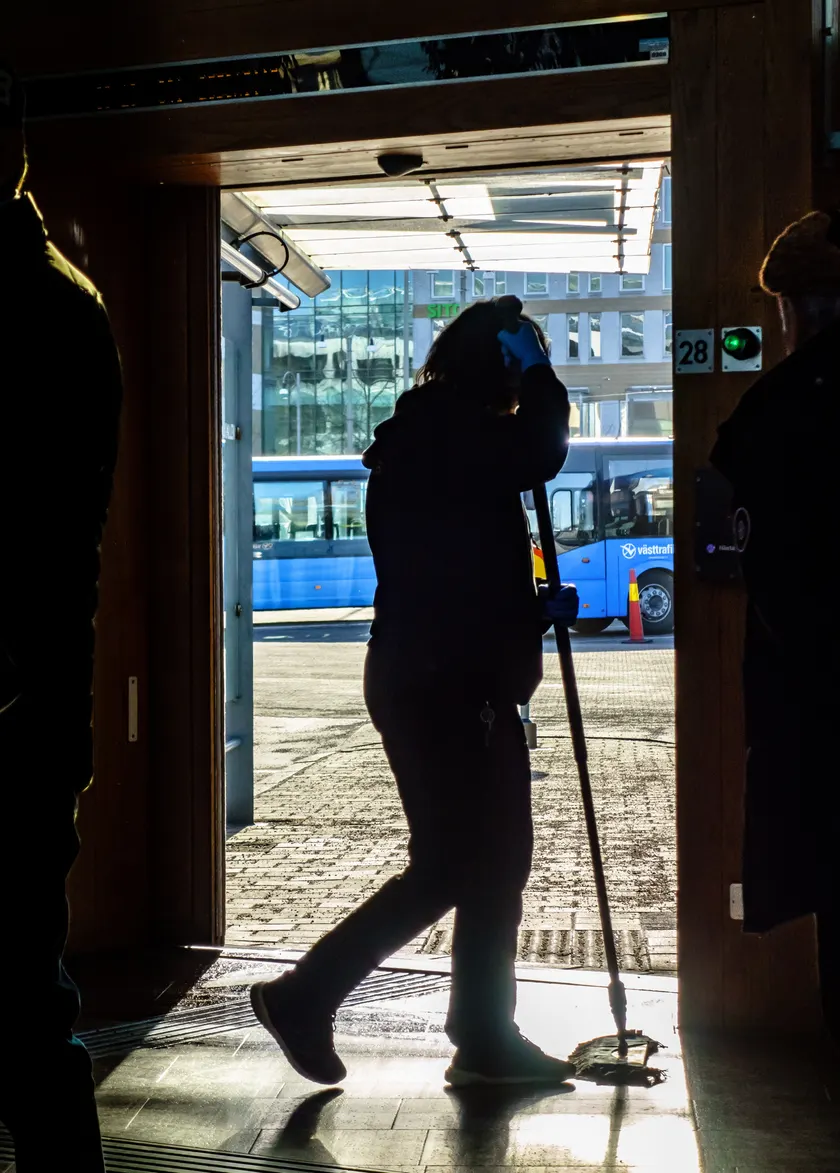 A cleaner in a yellow vest sweeping the floor of a large public terminal