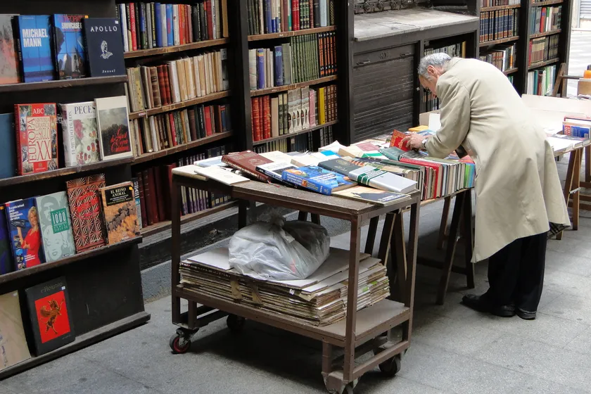 A person at an outdoor bookstall looking through a stack of books
