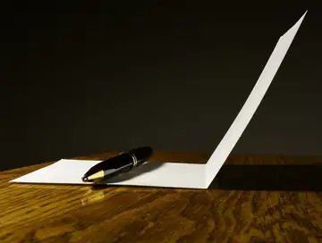 A fountain pen resting on a blank folded card on a wooden table